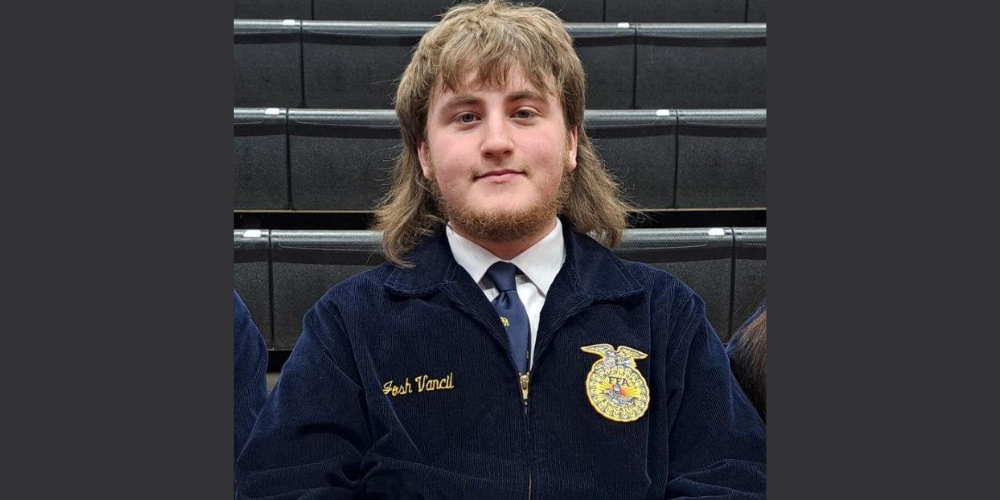 young man with light brown mullet and beard wearing a navy blue FFA jacket, white shirt, and navy tie